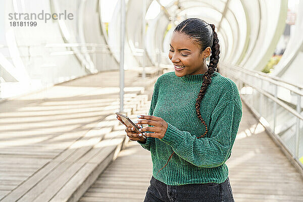 Glückliche junge Frau benutzt Smartphone auf Brücke