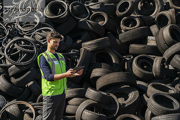 Mann benutzt Tablet-PC vor Gummireifen im Recyclingzentrum