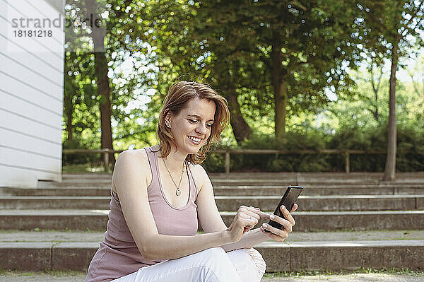 Glückliche Frau  die im Park Textnachrichten auf dem Smartphone sendet