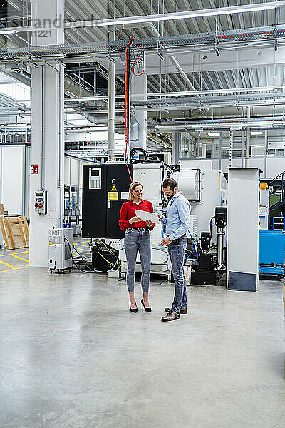 Geschäftsfrau hält Tablet-PC in der Hand und diskutiert mit Kollegen in der Fabrik