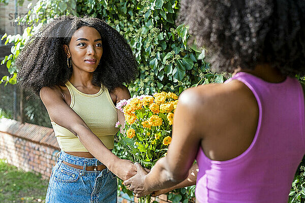 Lächelnde Frau mit Freundin hält Blumen auf Fußweg