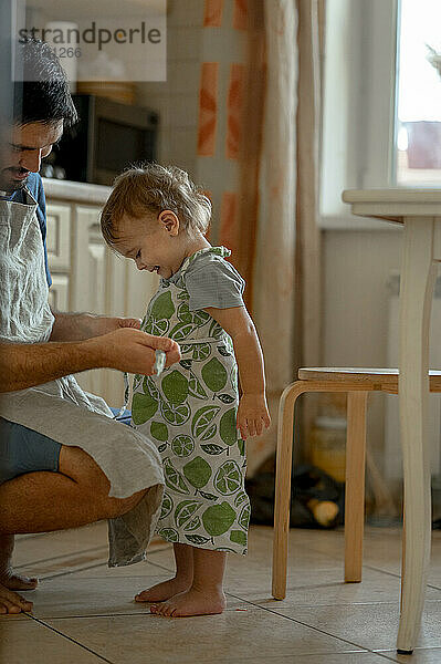 Vater bindet seinem kleinen Jungen in der heimischen Küche eine Schürze