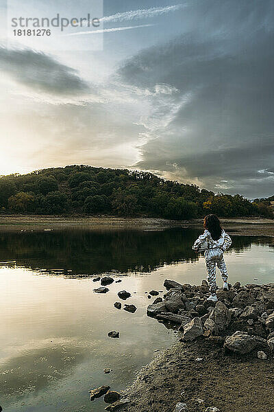 Astronaut holding space helmet standing on rock at beach
