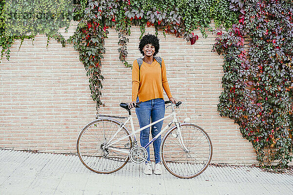 Lächelnde Frau mit Fahrrad vor Efeuwand