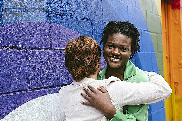 Lächelnde Frau umarmt Freund an bunter Wand