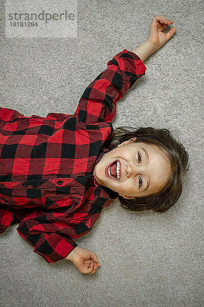 Cheerful boy wearing plaid shirt lying down on carpet