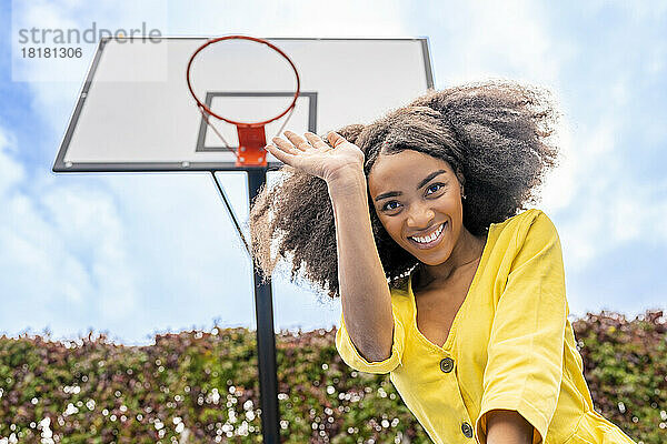 Glückliche junge Frau winkt vor dem Basketballkorb