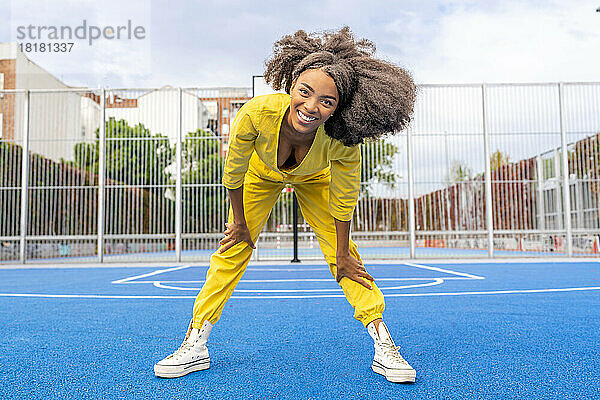 Glückliche junge Frau mit Afro-Frisur beugt sich auf dem Sportplatz