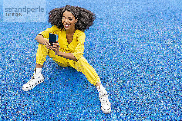 Glückliche junge Frau benutzt Smartphone auf blauem Basketballplatz