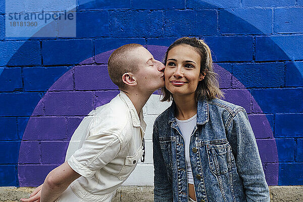 Nicht-binäre Person küsst junge Frau vor der Wand