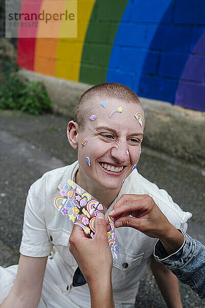 Woman sticking sticker on face of happy non-binary person