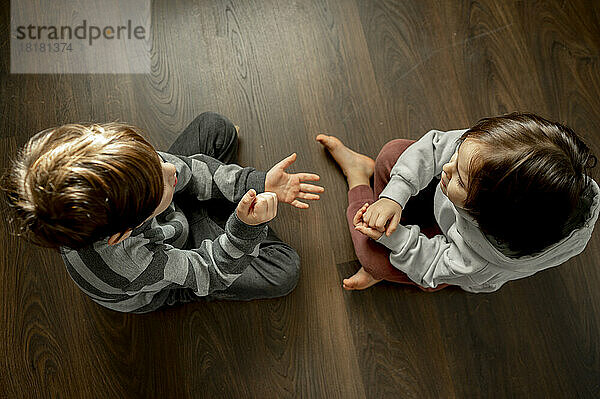 Junge und Bruder spielen zu Hause Steinpapierschere auf dem Boden