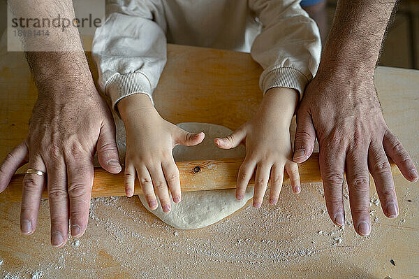 Hände von Sohn und Vater rollen Pizzateig in der Küche