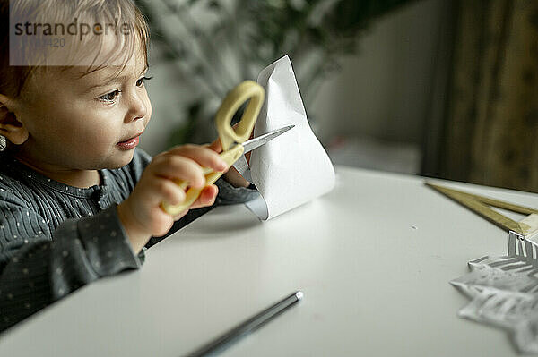 Junge schneidet Papier mit einer Schere am Tisch zu Hause