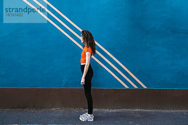 Junge Frau steht auf Fußweg vor blauer Wand