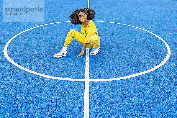 Junge Frau kauert auf blauem Basketballplatz