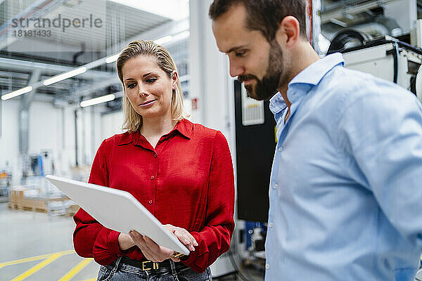 Lächelnde Geschäftsfrau teilt Tablet-PC mit Kollege in der Fabrik