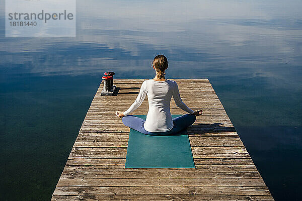 Frau meditiert an einem sonnigen Tag am Steg