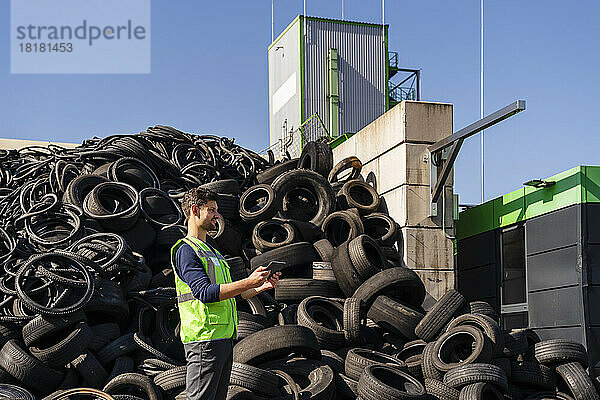 Mann mit Tablet-PC steht vor Gummireifen im Recyclingzentrum