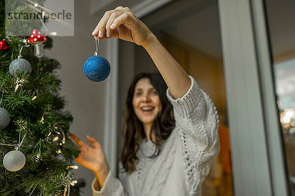 Frau hält Weihnachtsschmuck  um den Weihnachtsbaum zu schmücken