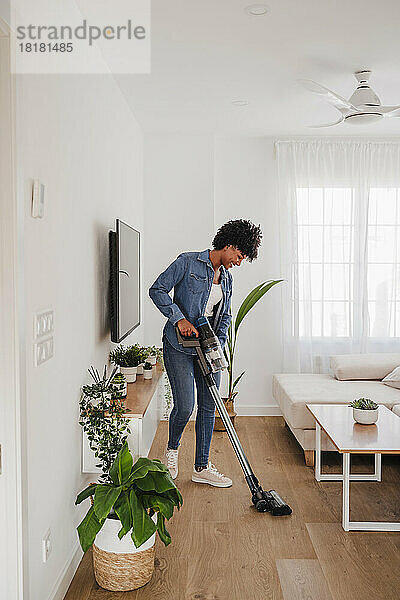 Frau reinigt Wohnzimmer mit Staubsauger zu Hause