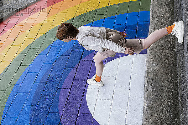 Young woman stepping on rainbow colored wall