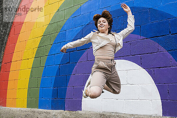 Junge Frau springt mit einer an die Wand gemalten Regenbogenfahne