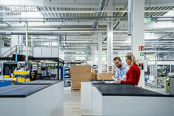 Lächelnde Geschäftskollegen benutzen Laptop auf dem Tisch in der Fabrik