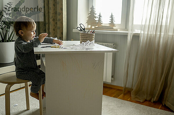 Kleiner Junge sitzt zu Hause auf einem Hocker neben dem Tisch