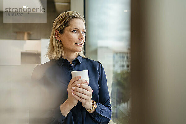 Nachdenkliche Geschäftsfrau mit Kaffeetasse im Büro