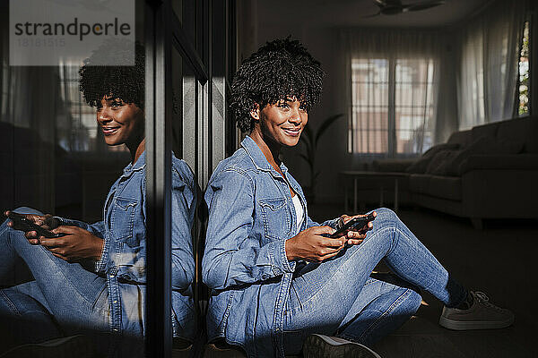 Lächelnde junge Frau mit Smartphone sitzt zu Hause im Wohnzimmer