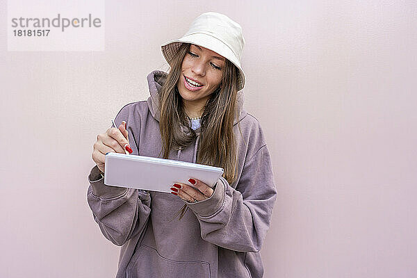 Frau mit Tablet-PC lehnt vor rosa Wand