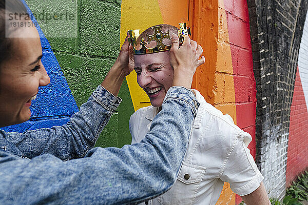 Lesbische Frau hält Krone auf Frauenkopf an Regenbogenwand