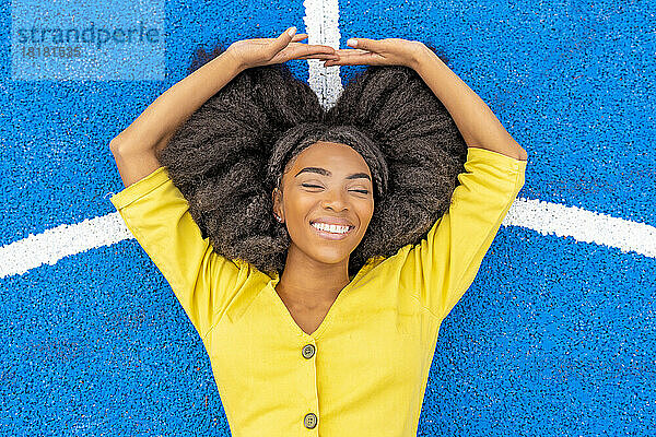 Happy young woman with eyes closed lying on blue basketball court