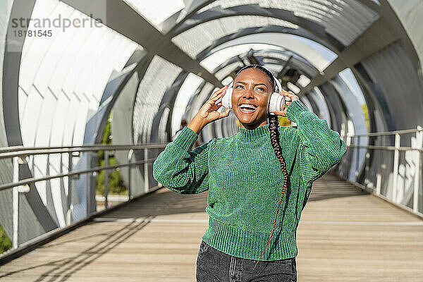 Glückliche junge Frau genießt Musik über kabellose Kopfhörer auf der Brücke