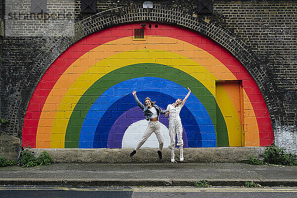 Fröhliches lesbisches Paar springt vor Wand