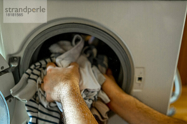 Hände eines Mannes  der Kleidung aus der Waschmaschine nimmt