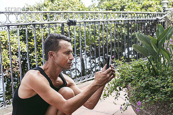 Mann fotografiert Pflanzen mit Smartphone in Pause auf Balkon