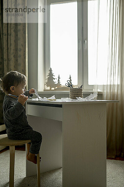 Junge sitzt zu Hause mit Papier und Bleistift auf einem Hocker