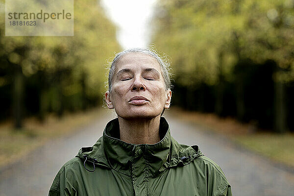 Ältere Frau mit geschlossenen Augen und Regenmantel