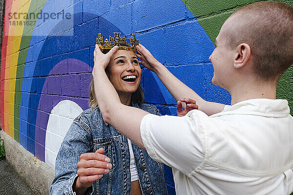 Nicht-binäre Person passt die Krone auf dem Kopf einer lesbischen Frau an der Regenbogenwand an