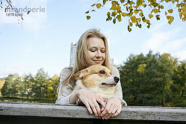 Lächelnde Frau und Hund lehnen sich im Park an ein Holzgeländer