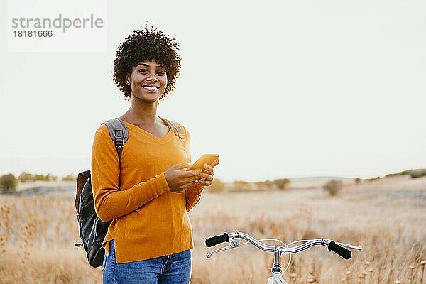 Lächelnde Frau mit Mobiltelefon mit dem Fahrrad im Feld