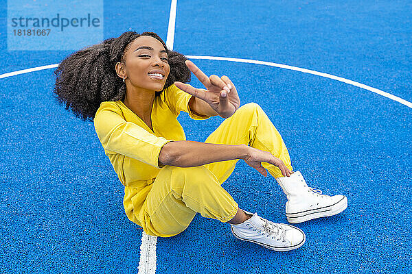 Happy woman gesturing peace sign sitting at sports court