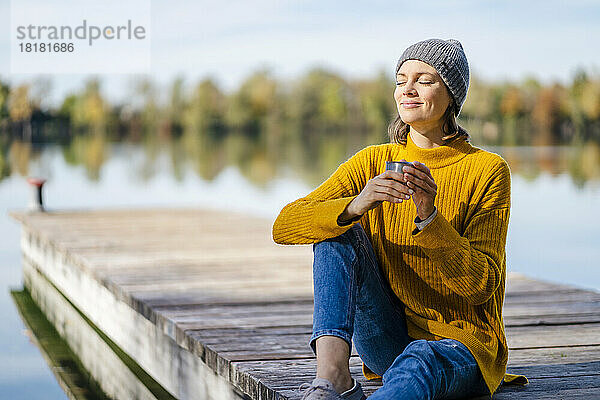 Lächelnde Frau sitzt an einem sonnigen Tag mit einer Kaffeetasse