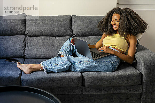 Relaxed Afro woman using laptop in living room at home