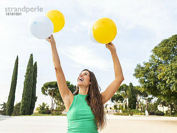 Glückliche Frau hält gelbe und weiße Luftballons am Fußweg