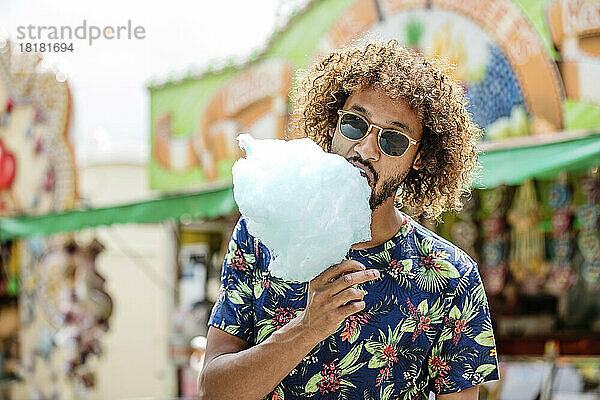 Junger Mann isst Zuckerwatte auf einem Jahrmarkt