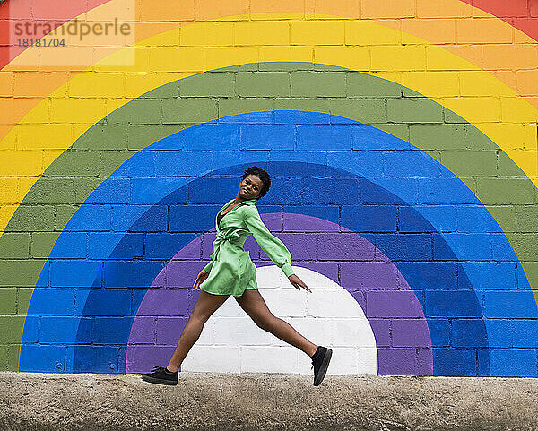 Frau springt vor einer an die Wand gemalten Regenbogenfahne