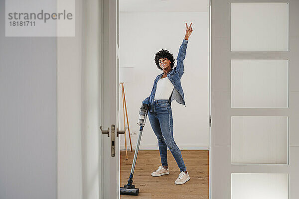 Glückliche junge Frau putzt Wohnzimmer mit Staubsauger